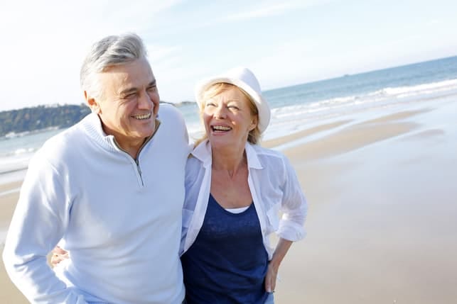 a senior couple dressed in white is having a walk on a beach