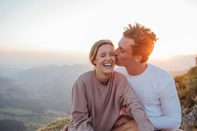 a man kissing his girlfriend’s cheek outdoors