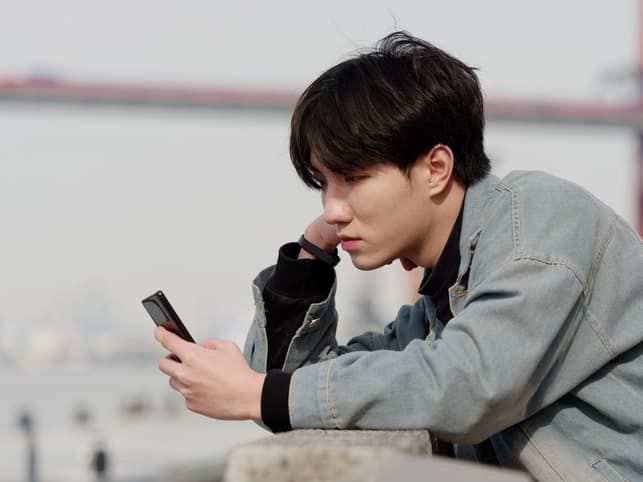 a young Asian man is using his smartphone outside