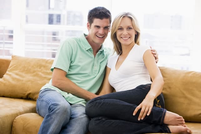 a couple posing together at home while sitting on a yellow sofa