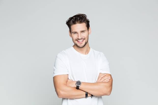 a young man in a white T-shirt posing with his arms crossed