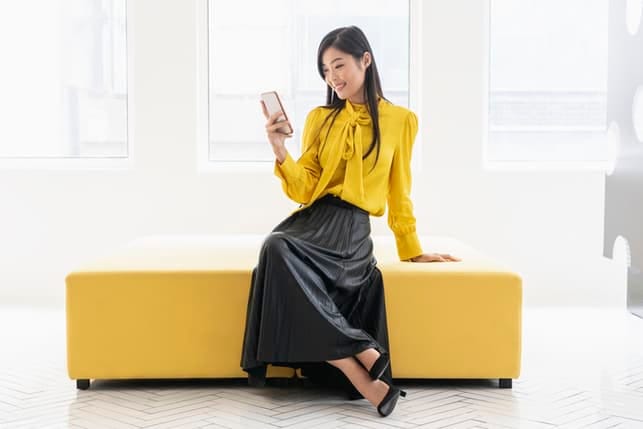 a young asian woman is yellow skirt is using her phone and smiling