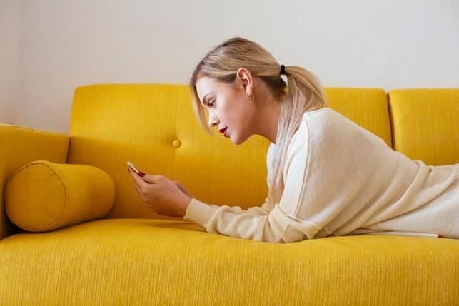 a young woman using her smartphone while lying on a yellow couch