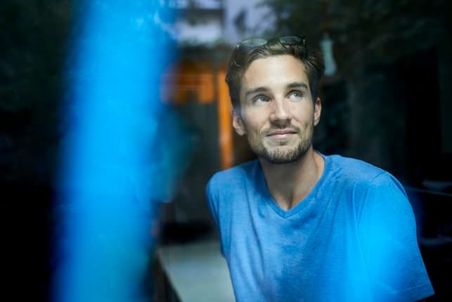 a man in a blue sweater thinking while sitting in a dark room