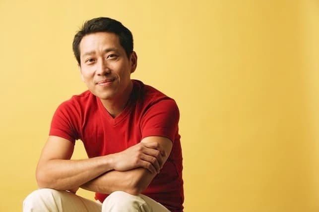 an asian man in red t-shirt is posing on a yellow background