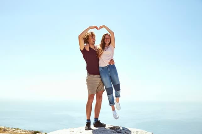a young couple making a heart sign on a beach