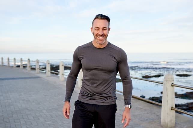 a sporty mature man is smiling while standing on a beach