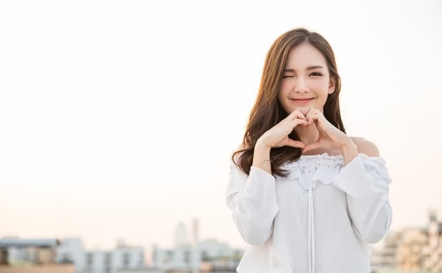 a young Asian girl making a heart sign with her fingers