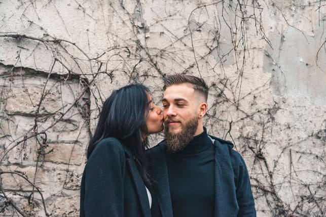 a young mixed couple wearing black is kissing outdoors